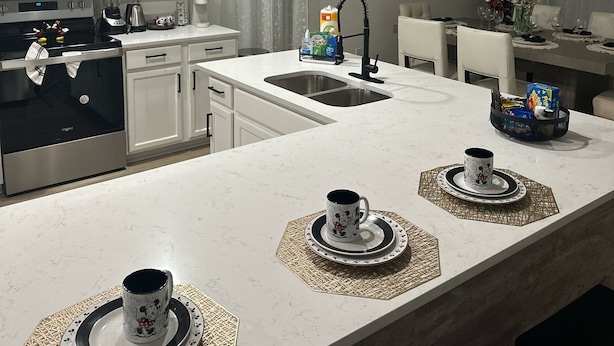 Una cocina moderna con armarios blancos, un microondas, una estufa y un lavamanos. Hay individuales sobre la encimera y un ventilador de techo.