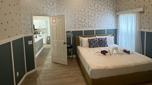 Un dormitorio con cama, mesita de noche, cómoda y baño visible a través de una puerta abierta.