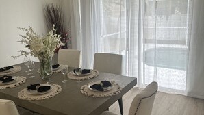 Comedor con una mesa dispuesta para cuatro, sillas blancas, ventilador de techo y cortinas de gasa.