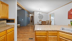 A kitchen with wooden cabinets, a granite countertop, a dining area with a chandelier, and a wall-mounted clock. - Big Parking Lot, Pets Invited, Fenced Farm Home (Kennewick)