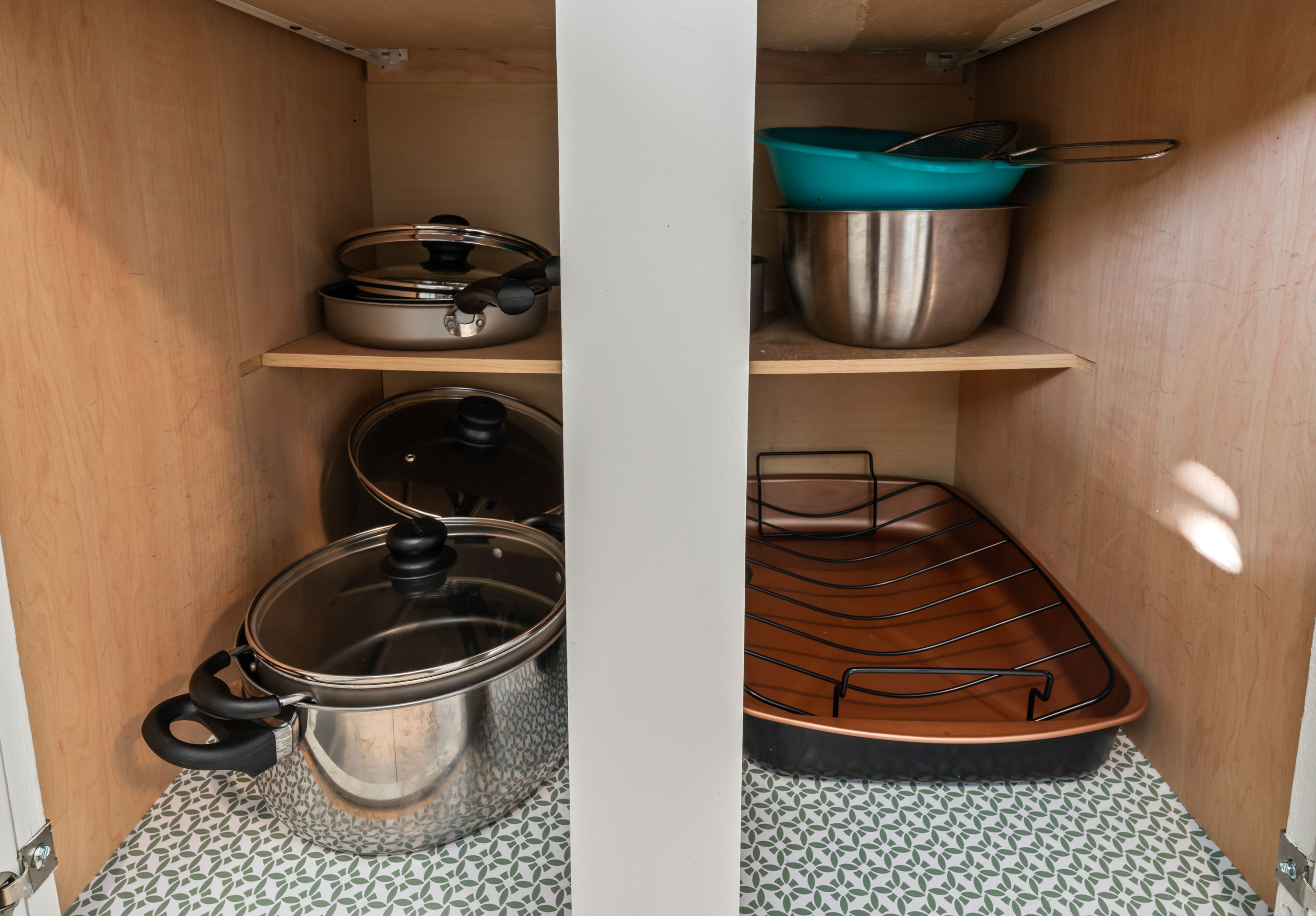 Una cocina con ollas y sartenes de acero inoxidable en estantes, una olla azul en el estante superior y una rejilla en el estante inferior.