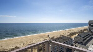 A beach view from a balcony with a clear sky, sandy beach, and a building with a parking lot. - Sea Terrace 88th St, Outdoor Pool, Oceanfront building & View, *FREE Linen Pkg* (Ocean City)
