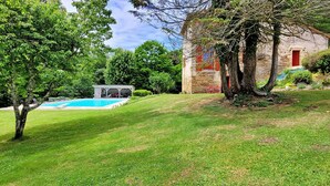 A grassy area with a swimming pool, a stone building with a red door, and trees. - Beautiful home in St Paul La Roche (St Paul La Roche)