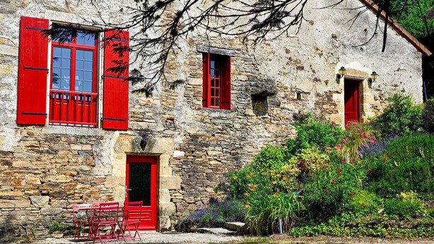 A stone building with red shutters and a door, a small window, and a garden with various plants. - Beautiful home in St Paul La Roche (St Paul La Roche)