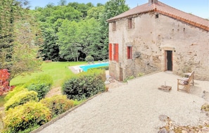 Un bâtiment en pierre doté d’une piscine, entouré d’une végétation luxuriante.