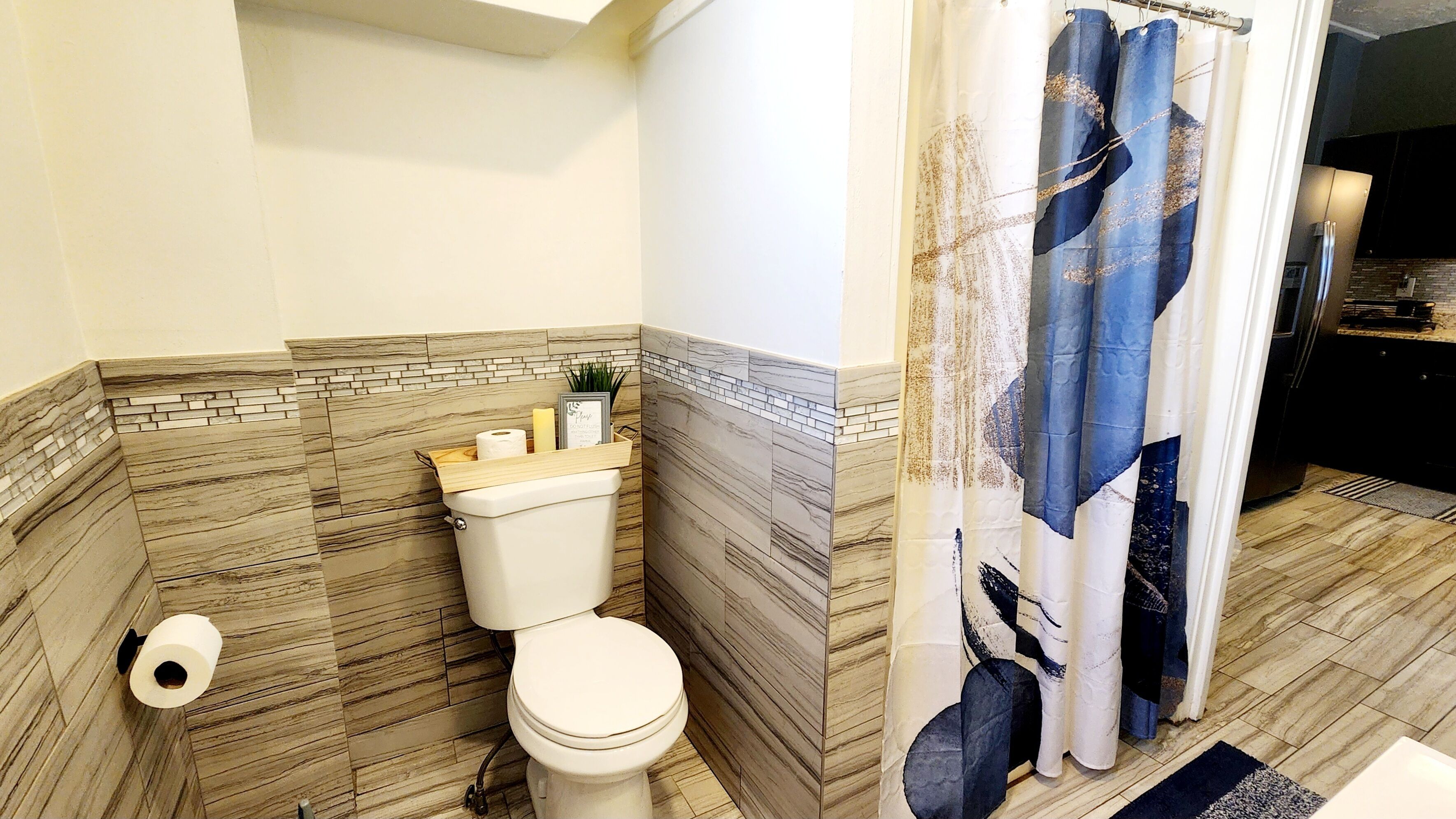 A bathroom with a toilet, a shower curtain, and a tiled wall.