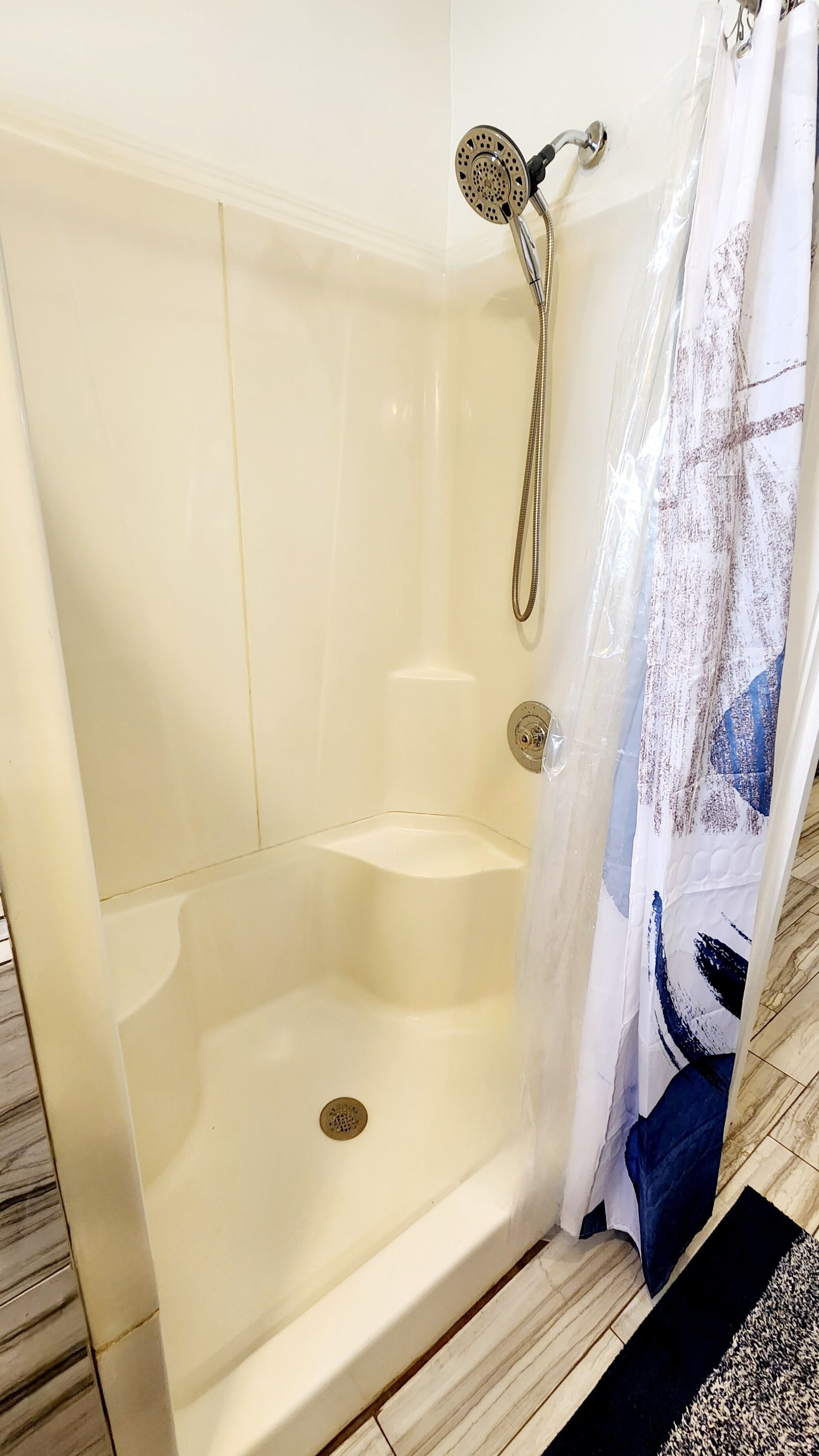 Une douche à l’italienne avec une porte en verre, un pommeau de douche amovible et un drain.