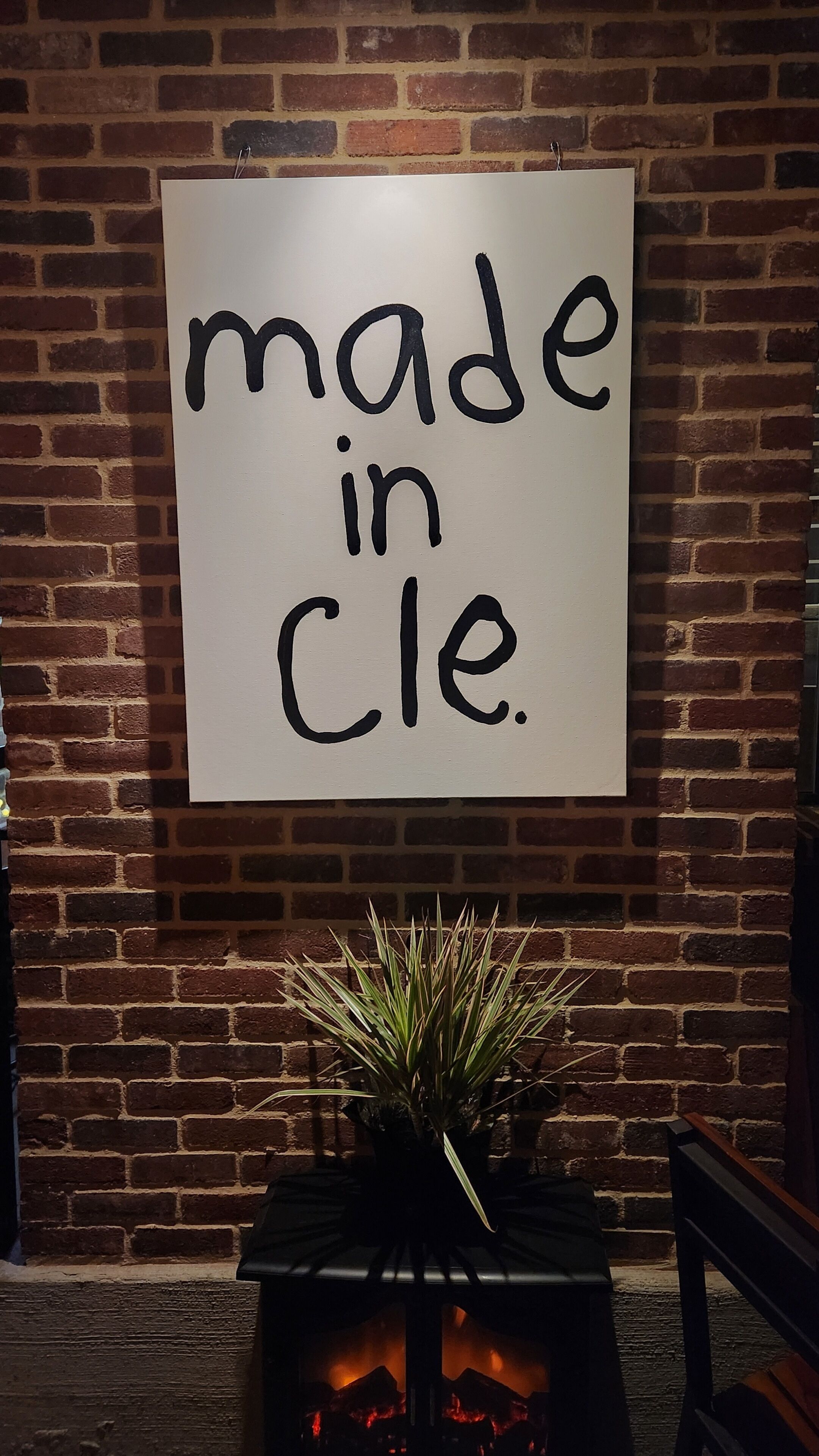 A sign with the text 'made in Cle.' mounted on a brick wall.