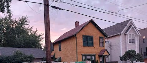 A residential street with houses, a colorful mural on a fence, and a parked car.