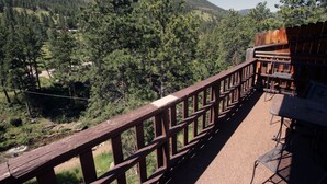 A wooden deck with outdoor seating overlooking a forested valley and a mountain. - Studio Style Condo with Full Kitchen and Spacious Deck (Estes Park)