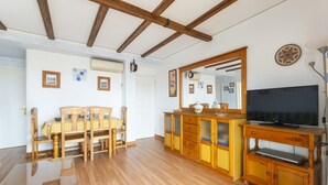 A room with wooden flooring, a dining table with chairs, a wooden cabinet with a television, and a mirror on the wall. - LES GAVINES - Charming apartment with sea views - Free Wifi (Dénia)