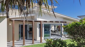 A modern house with a covered patio, glass doors, and a well-maintained lawn. - Coastal charm on Casuarina Way with a pool! (Tweed)