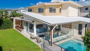 A modern house with a large glass-enclosed patio and a swimming pool. - Coastal charm on Casuarina Way with a pool! (Tweed)