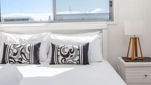 A hotel room with a bed, two patterned pillows, a bedside lamp, and a window with a view of a snowy landscape. - Coastal charm on Casuarina Way with a pool! (Tweed)