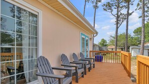 A wooden deck with Adirondack chairs, a wooden railing, and a view of a building with a blue door.
