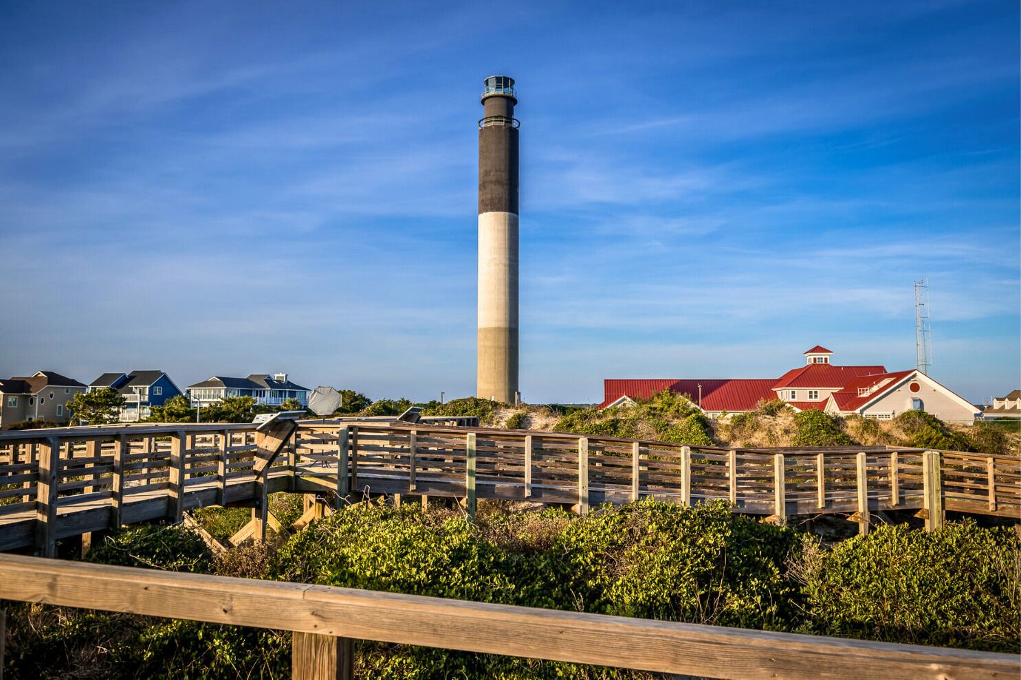 A coastal area with a prominent lighthouse, wooden boardwalks, and residential buildings with red roofs.