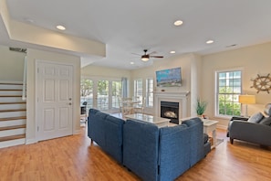 A spacious living room with a fireplace, a ceiling fan, and a large window.