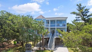 A two-story building with a balcony, a covered porch, and a pathway leading to the entrance. - "Pearl on a Strand" 6Bd/4Ba w/ Pool, Opt Golf Cart (Oak Island)
