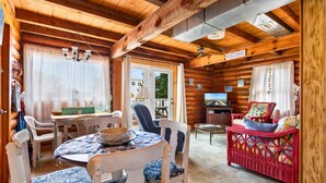 A cozy log cabin interior with a dining area, a seating area with a TV, and a balcony with a view.