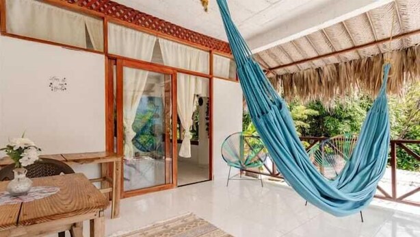 A room with a wooden table, a hanging hammock, and a view of greenery outside. - Hotel talu  tayrona (Santa Marta)