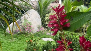 A tropical garden with large rocks, lush greenery, and a thatched-roof structure. - Hotel talu  tayrona (Santa Marta)