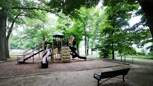 Une aire de jeux avec un toboggan, des structures d’escalade et un banc dans un parc.