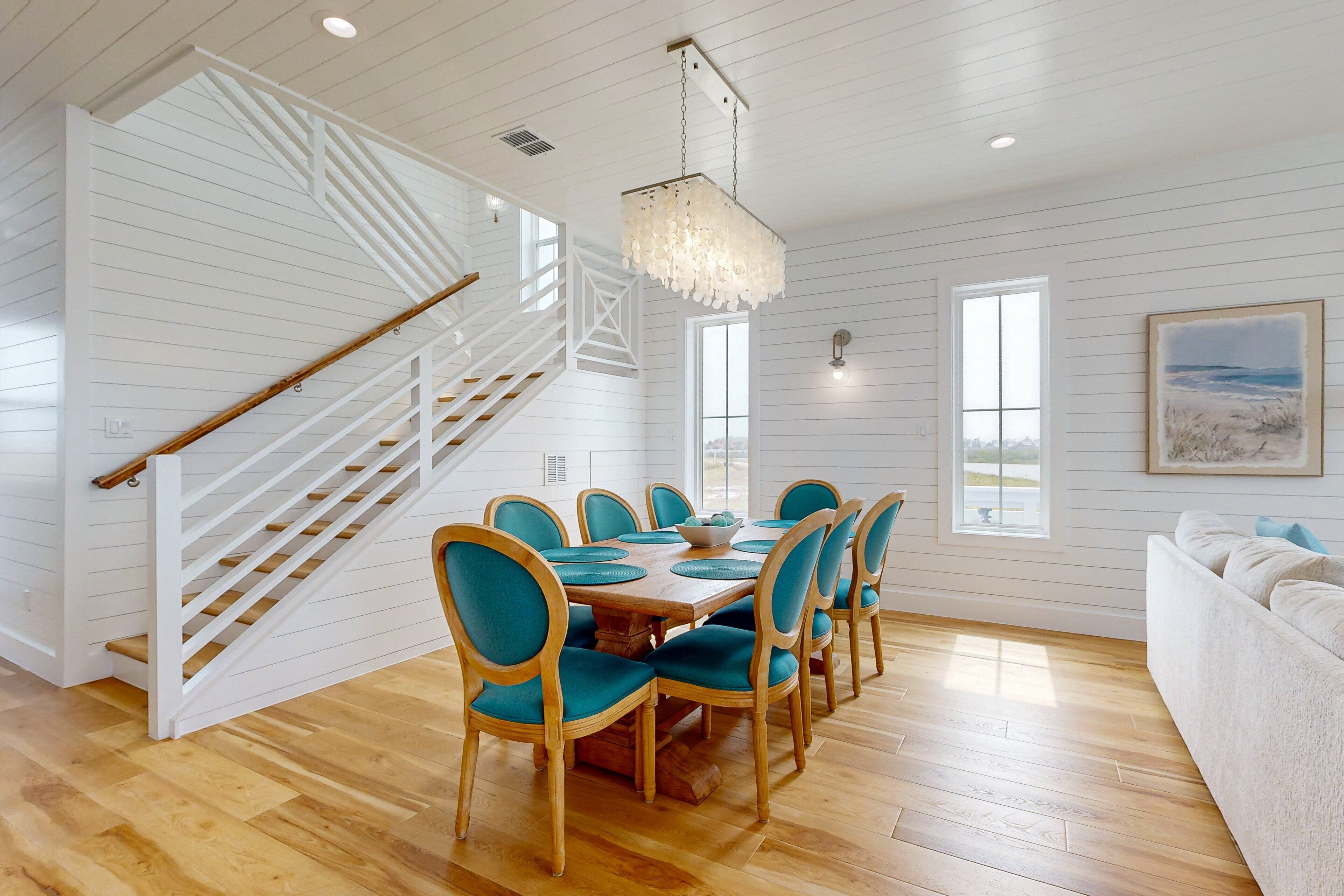 Un espace repas avec une table et des chaises en bois, un escalier et une vue sur l’extérieur.