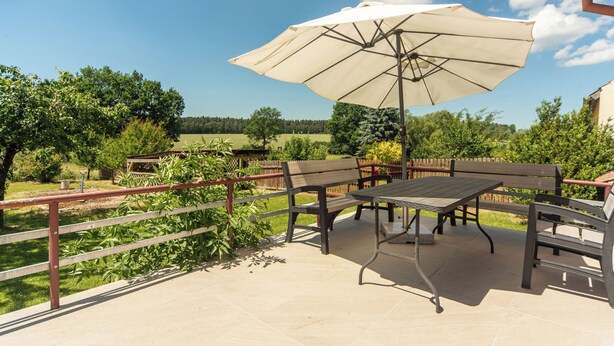An outdoor patio with a table and chairs, a large umbrella, and a view of the surrounding landscape.