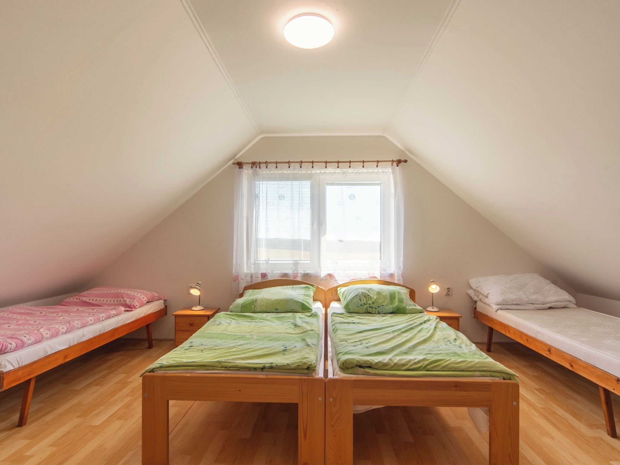 Habitación tipo dormitorio con dos camas individuales, suelo de madera, luz en el techo y una ventana con cortinas.