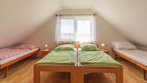 A dormitory room with two single beds, a wooden floor, a ceiling light, and a window with curtains.