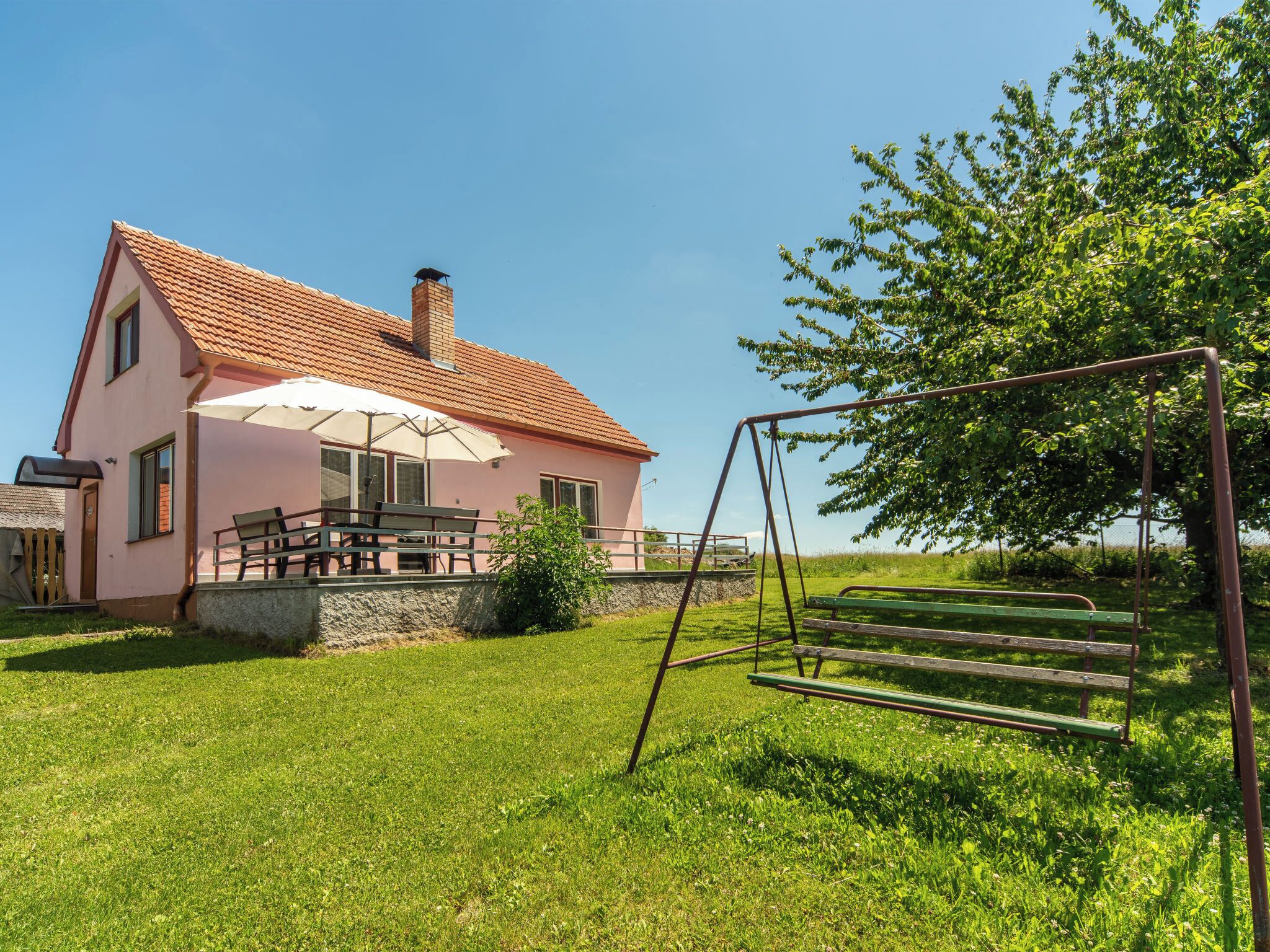 A pink house with a red-tiled roof, a swing set, and a bench in a grassy yard.
