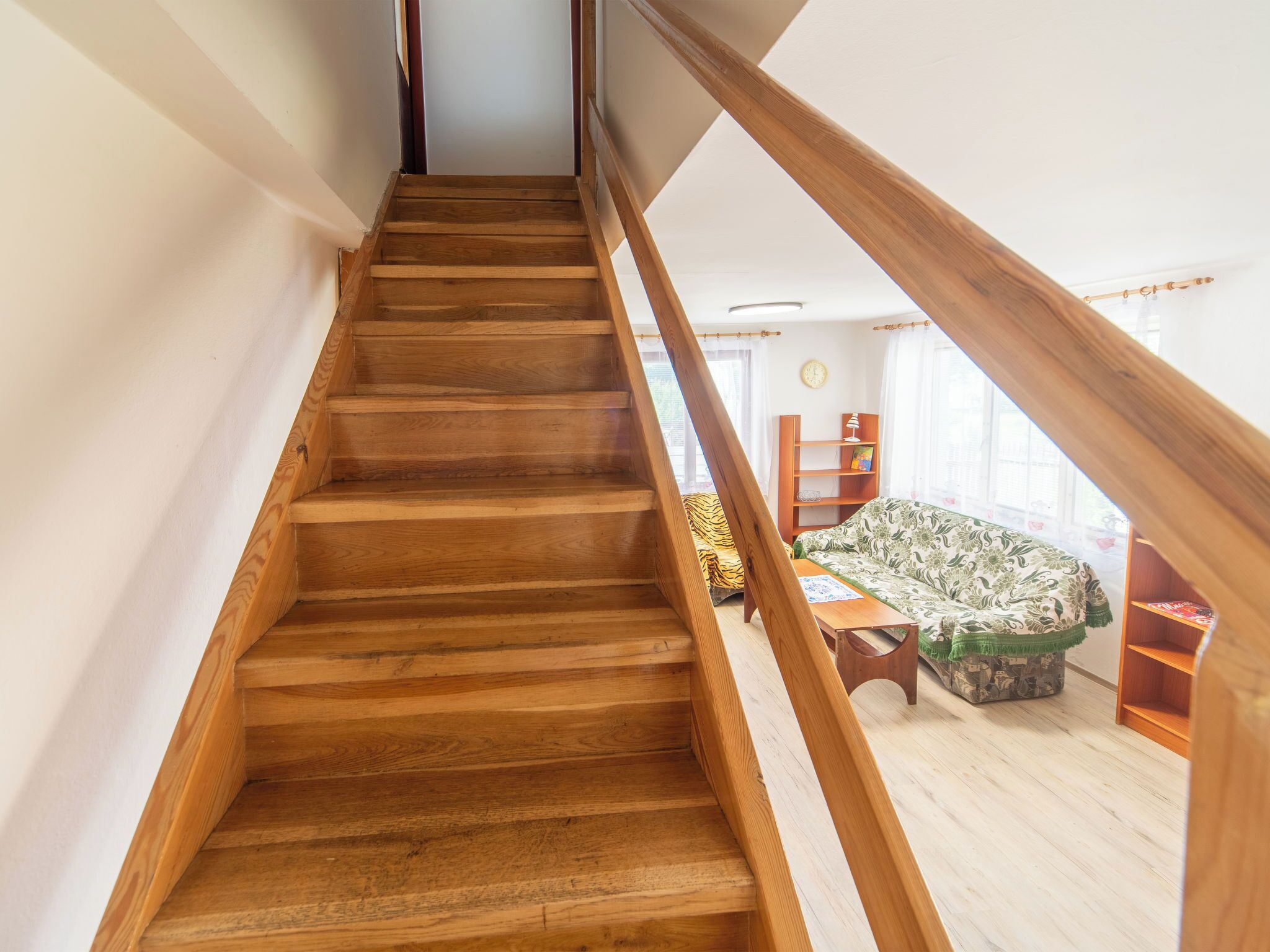 Una escalera de madera que lleva a un dormitorio en el altillo con vistas al exterior.
