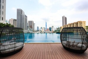 A rooftop pool area with two black wireframe chairs, a wooden deck, and a city skyline view in the background. - Sentral Suites KL Sentral By Luxe Home (Kuala Lumpur)