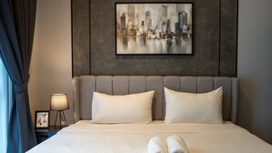 A hotel room with a large bed, two pillows, a framed cityscape painting, a nightstand with a lamp, and a framed picture. - Sentral Suites (Kuala Lumpur)