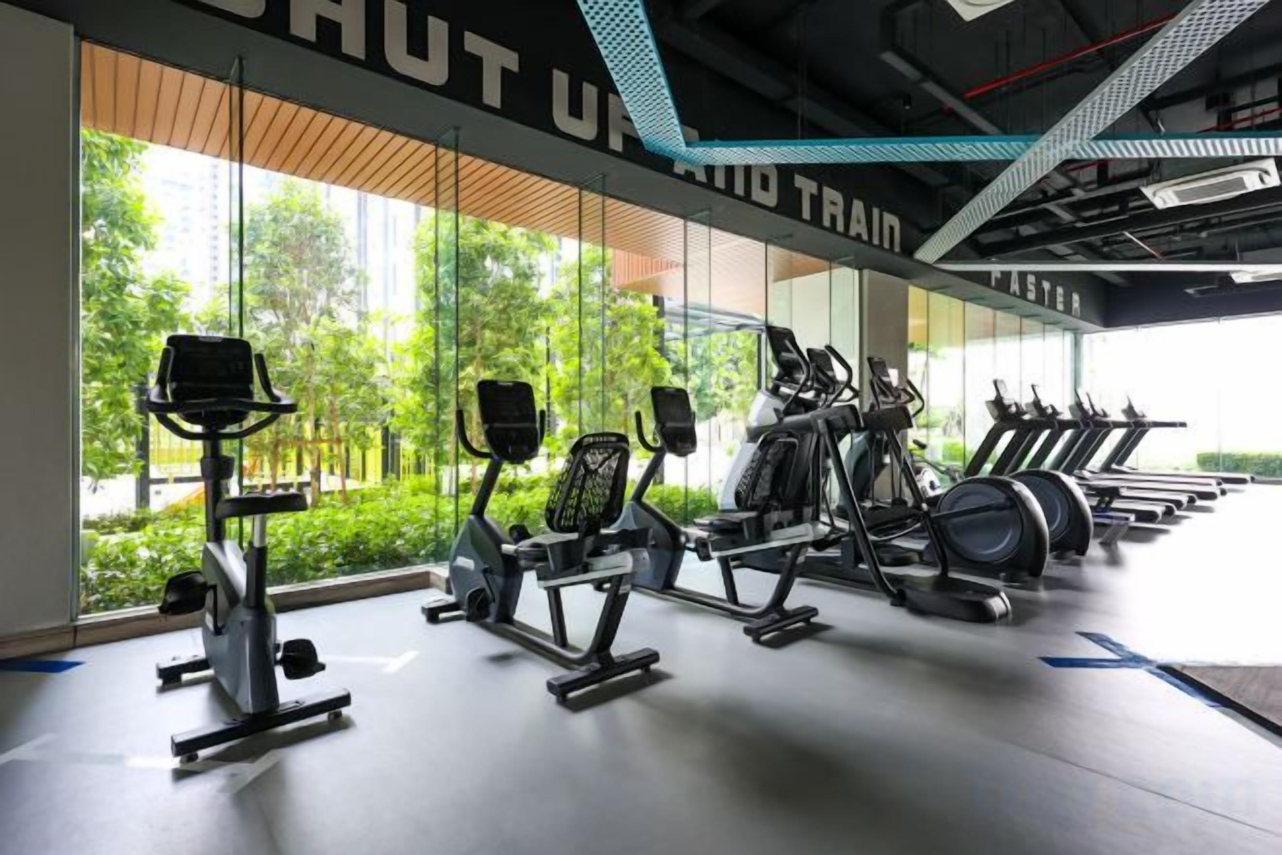 A gym with various exercise equipment, large windows, and a view of greenery outside.