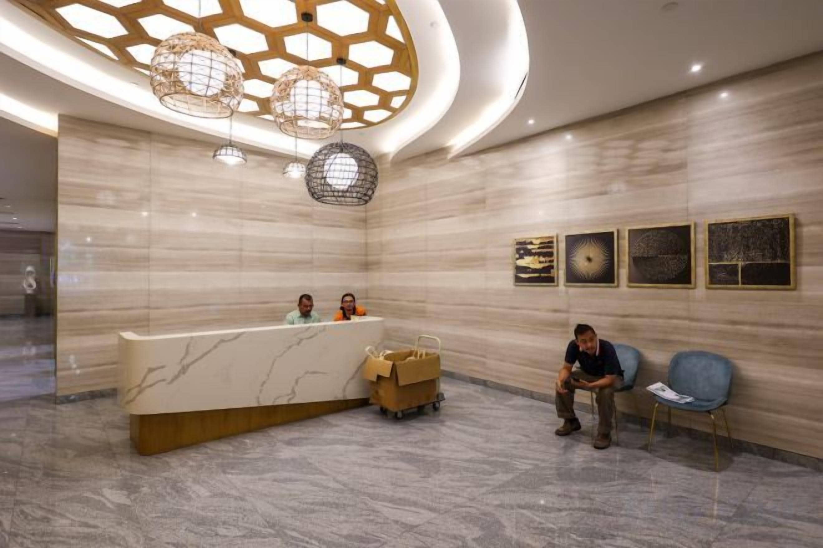 A hotel reception area with a marble reception desk, a waiting area with chairs, and a ceiling with a geometric light fixture.