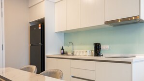A modern kitchen with white cabinets, a black refrigerator, a coffee maker, and a light blue backsplash. - Sentral Suites (Kuala Lumpur)