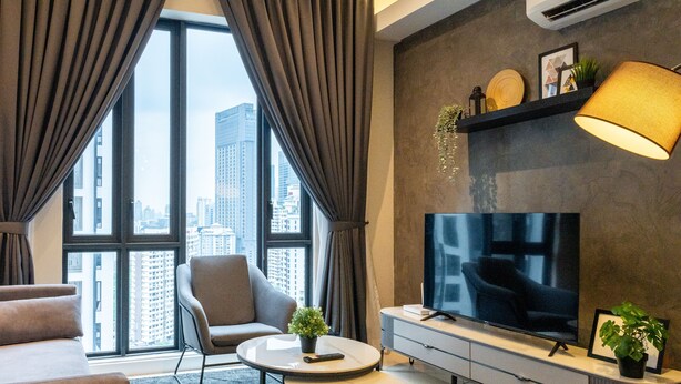 A modern living room with a large window, a flat-screen TV, a sofa, a chair, and a coffee table. - Sentral Suites (Kuala Lumpur)