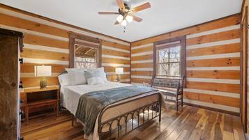 Un dormitorio tipo cabaña de madera con una cama, dos mesitas de noche, un ventilador de techo y una ventana.