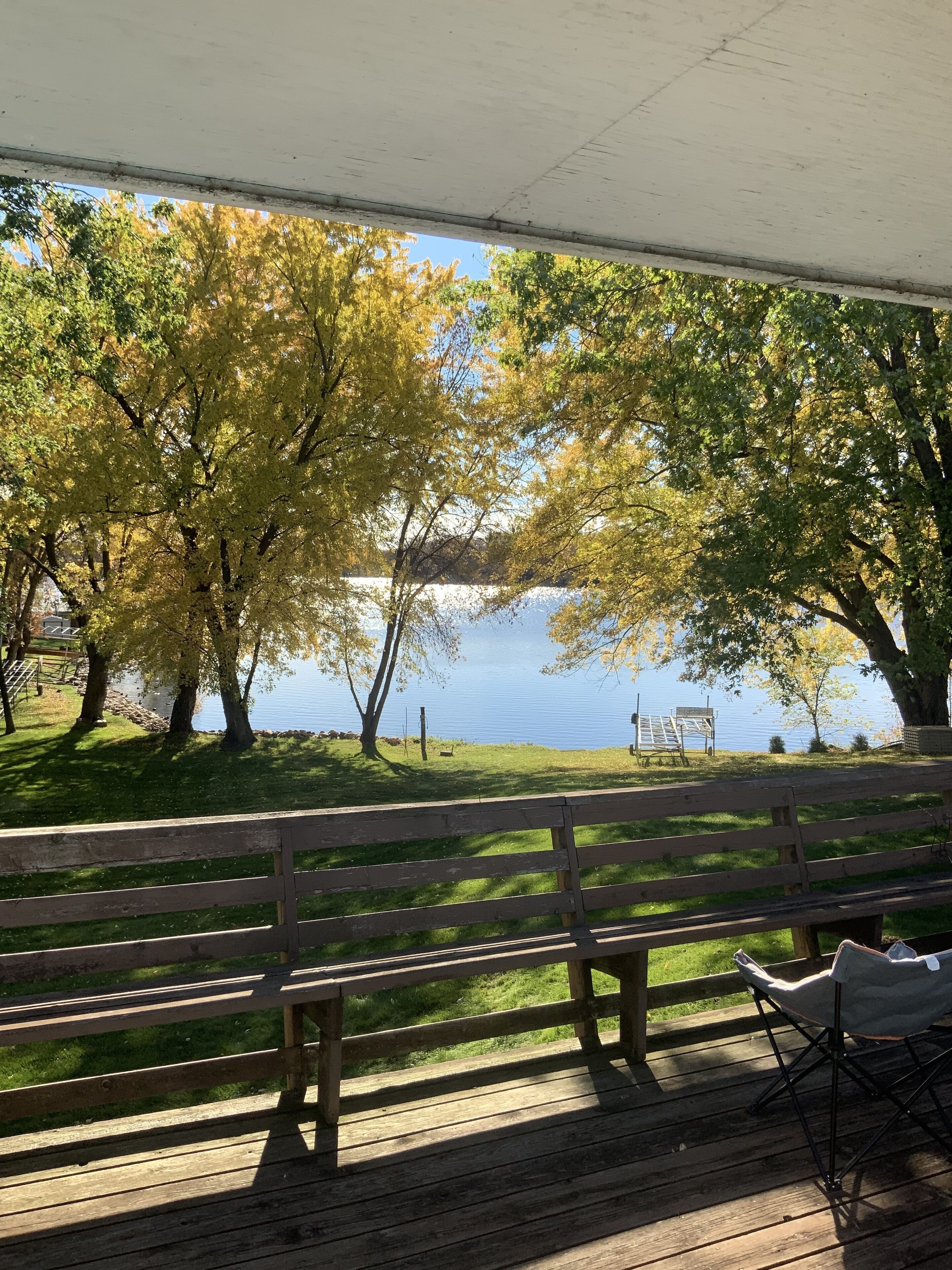 Eine Holzterrasse mit Bänken, die auf einen See mit Blick auf Bäume mit gelben Blättern blickt.