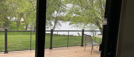 Blick von einem Zimmer mit einer Holterrasse auf einen See, mit Metallgeländer und einer Hängematte.