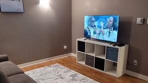Un saló amb un sofà, una taula de centre de vidre, una televisió sobre un moble, una catifa estampada i terres de fusta.