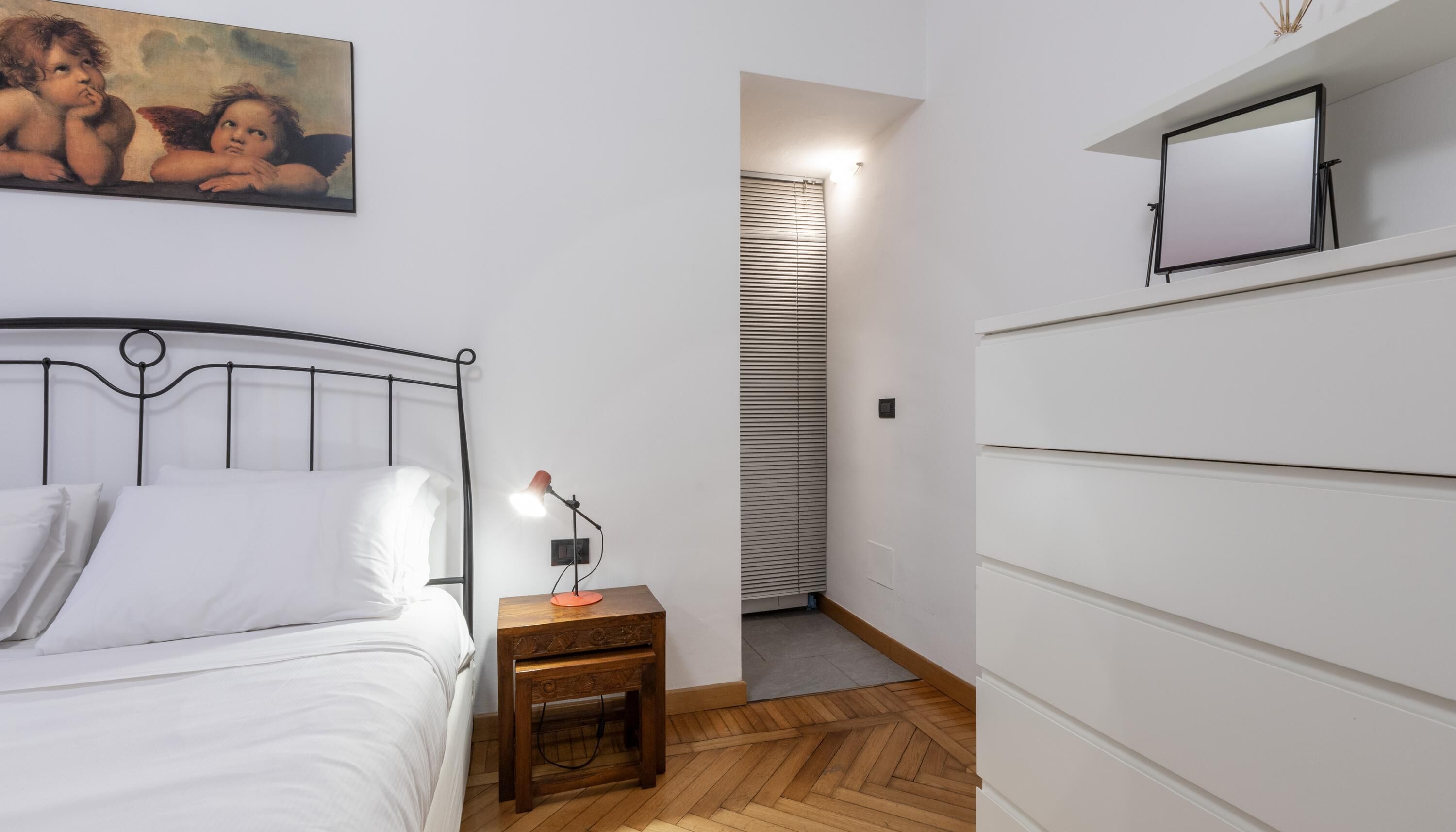 A bedroom with a bed, bedside table, lamp, and a painting on the wall.
