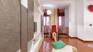 A modern living room with a TV, a dining area with a table and chairs, and a red heart-shaped clock on the wall. - Italianway Easy - Masotto 4 (Milan)