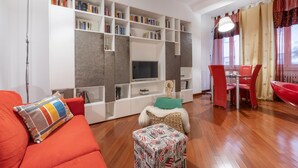 A living room with a red sofa, a small ottoman, a television, and a bookshelf filled with books. - Italianway Easy - Masotto 4 (Milan)