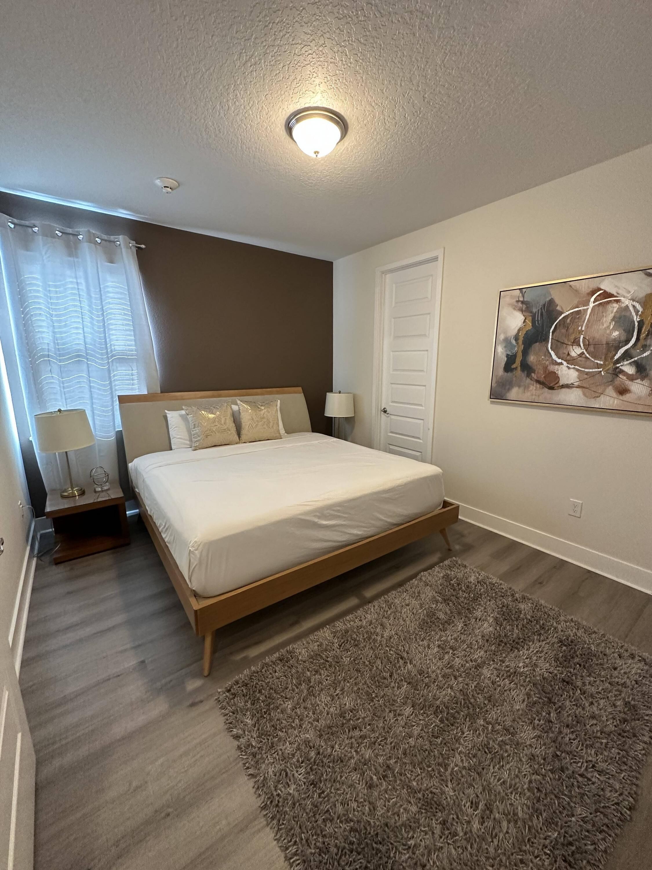 A bedroom with a bed, nightstands, a lamp, a door, and a painting on the wall.