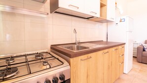 Una cocina con estufa a gas, pileta de acero inoxidable, muebles de madera y refrigerador blanco.