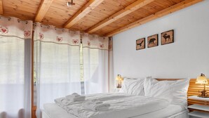 A bedroom with a bed, white bedding, wooden headboard, bedside lamps, and wall art of animals.