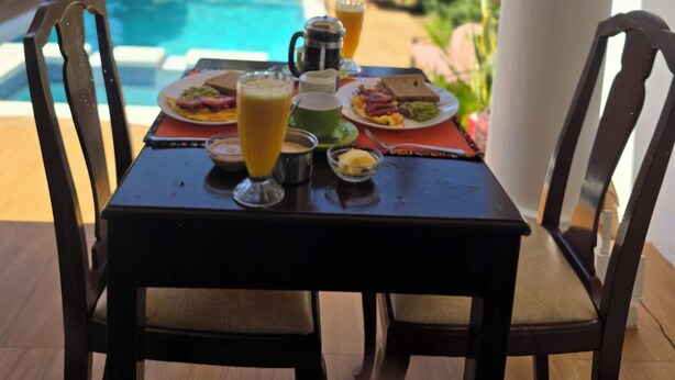 A dining table with breakfast items and a view of a swimming pool and palm trees. - Sprunger Avenue-Tulia Homes  (Moshi)