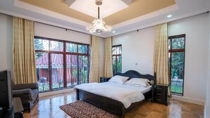 A bedroom with a large bed, a TV, and a chandelier. - Sprunger Avenue-Tulia Homes  (Moshi)